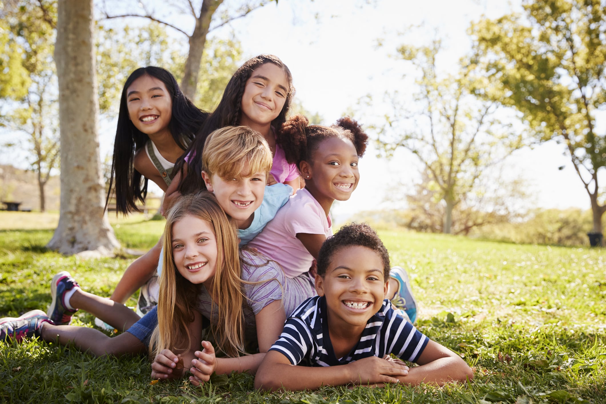 Multi-ethnic group of kids lying on each other in a park